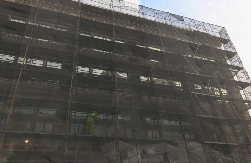 scaffold on the side of a large building with construction workers
